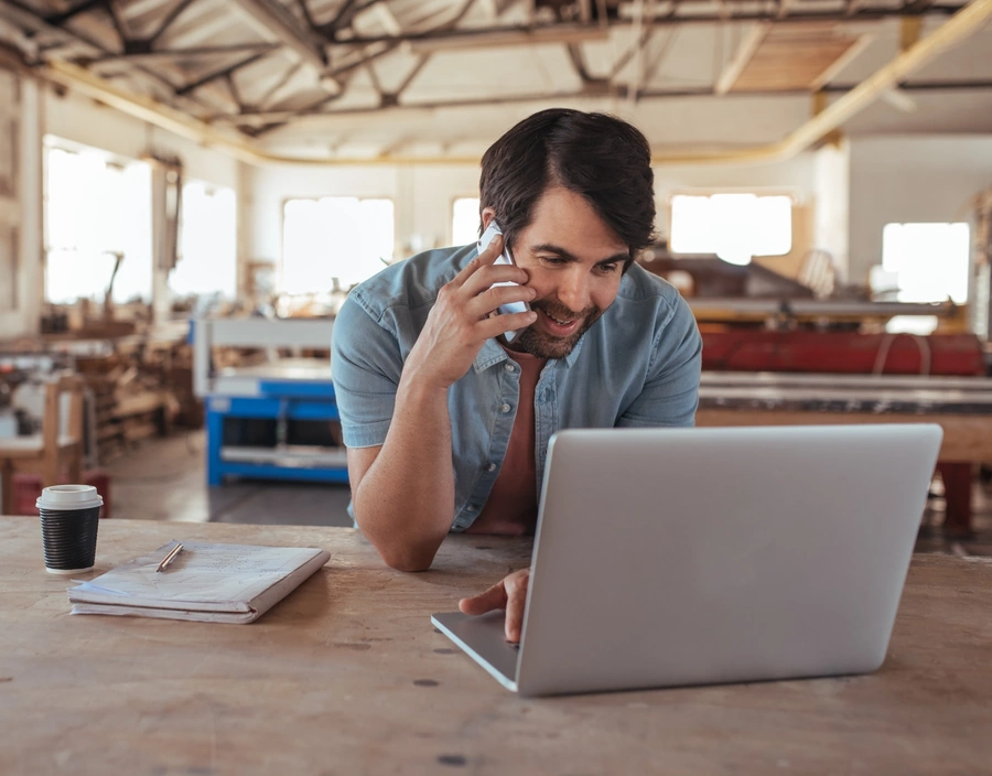 Man talking on the phone and using a laptop in a workshop.