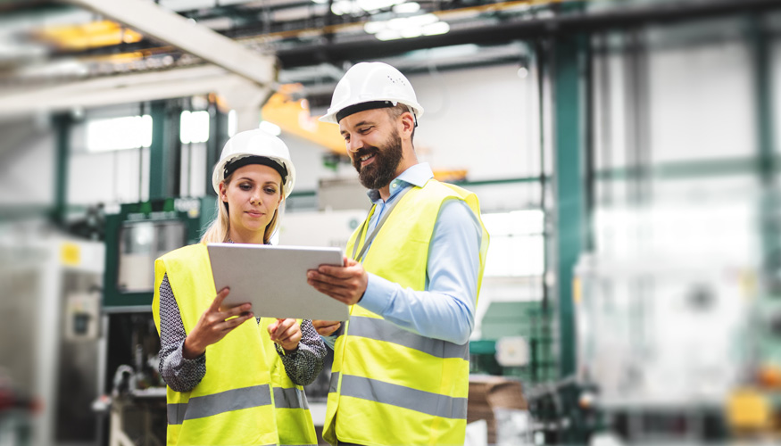 A portrait of an industrial man and woman engineer with tablet in a factory, talking.