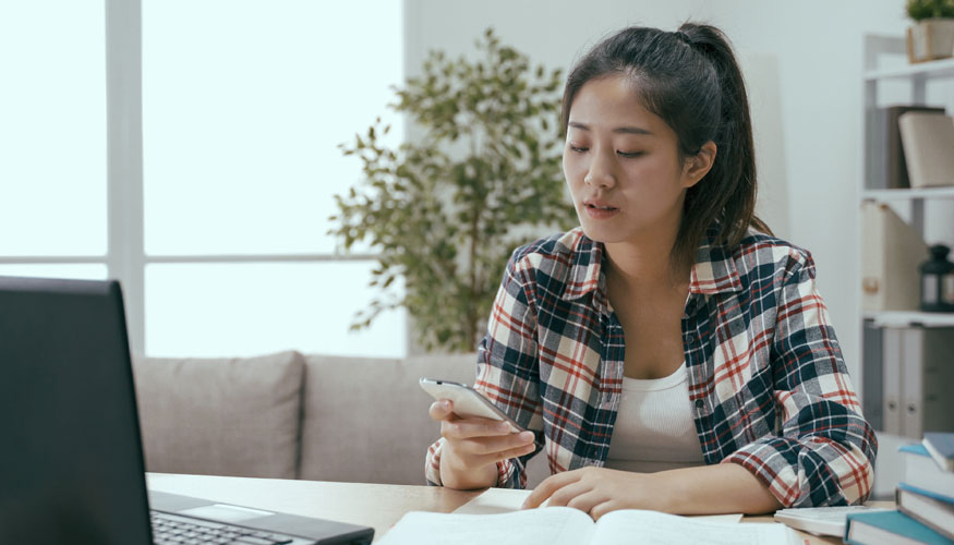 asian chinese young woman is preparing for test and having mobile phone online conversation at the same time